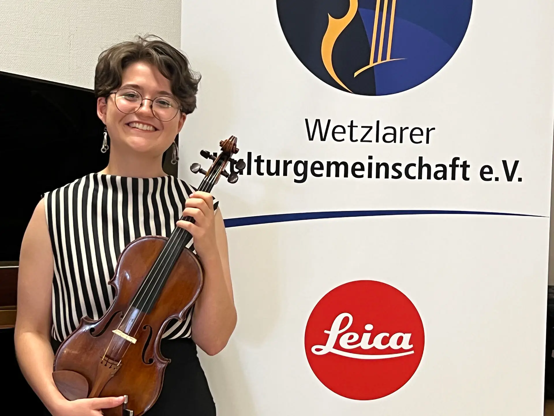 Elsie Kühn-Leitz Stipendium 2026/27; Varvara Vasylieva mit Geige vor Plakat der Wetzlarer Kulturgemeinschaft